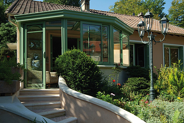 En appui en façade, cette véranda affiche une couleur verte qui rappelle celle de la nature environnante. Reynaers.