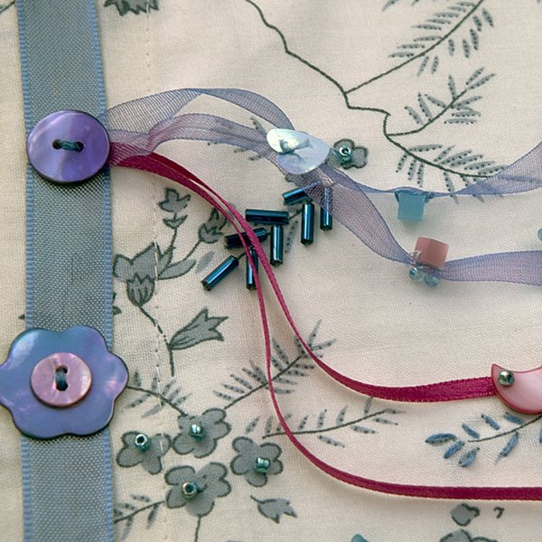 Décorer les motifs de  boutons, de perles et  de feuilles brodées.
