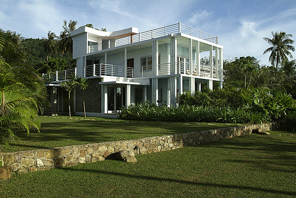 Le bâtiment bleu est ouvert sur de larges terrasses qui offrent une magnifique vue sur l’océan. Le jardin planté d’orchidées rares, de fougères arborescentes, de bambous et de palmiers laisse de vastes espaces plantés d’herbes descendant jusqu’à la grève