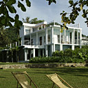 Le bâtiment bleu est ouvert sur de larges terrasses qui offrent une magnifique vue sur l’océan. Le jardin planté d’orchidées rares, de fougères arborescentes, de bambous et de palmiers laisse de vastes espaces plantés d’herbes descendant jusqu’à la grève