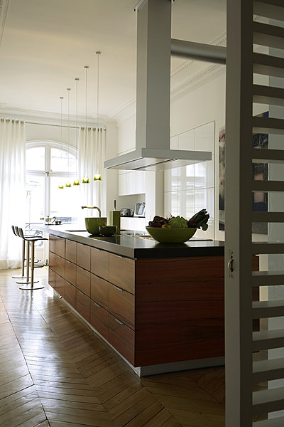 Le grand comptoir de 7 m s’étend d’un bout à l’autre de la cuisine ouverte. Il est souligné de granit Nero flammé. Les deux éviers se font face. Les grands placards et tiroirs contiennent toute la batterie de cuisine. Suspensions Philip Starck chez Flos