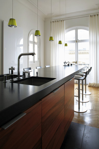 Le grand comptoir de 7 m s’étend d’un bout à l’autre de la cuisine ouverte. Il est souligné de granit Nero flammé. Les deux éviers se font face. Les grands placards et tiroirs contiennent toute la batterie de cuisine. Suspensions Philip Starck chez Flos