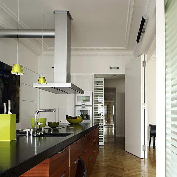 Le grand comptoir de 7 m s’étend d’un bout à l’autre de la cuisine ouverte. Il est souligné de granit Nero flammé. Les deux éviers se font face. Les grands placards et tiroirs contiennent toute la batterie de cuisine. Suspensions Philip Starck chez Flos