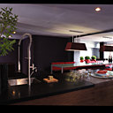 L’espace salle à manger-cuisine s’impose sur une très grande surface, les meubles en plaquage d’ébène couvert de pierre Belfast noir s’intègrent parfaitement dans ce décor épuré. Verres soufflés et assiettes thermoformées Exsud