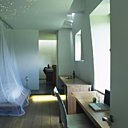 Ouvrant sur la salle de bains, l’ambiance “lit à baldaquin” de l’une des chambres est subtilement proposée par un jeu de tulle suspendue sur des rails en acier brossé et par les leds formant un petit halo romantique dans le plafond. Draps en lin Eden Park