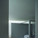 Une chambre présentée avec une autre sorte de lit à baldaquin en bois, adossé à une cloison grise derrière laquelle se cache la salle de bains. Draps Eden Park