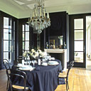 La salle à manger surprend par ses contrastes et ses jeux de reflets. De couleur noire, les murs, les meubles et la nappe mettent en valeur la vaisselle immaculée, l’argenterie et le lustre en cristal