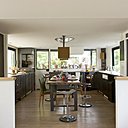 Deux petits murets marquent la séparation entre la cuisine et le salon. Portes de placards, portes, ouvertures, suspensions, table, Evasion 55 ; tabourets de tracteurs chinés, chaises vertes, Emmaüs.