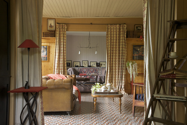 Une enfilade de pièces très raffinée où chaque objet et meuble trouve sa place tel un décor : des rideaux, Editions Chotard, posés sur une tringle artisanale  viennent délimiter chaque pièce ; devant la cheminée un magnifique Chesterfield , Village Notre Dame, table basse, Thonet ; petite table rouge, RKR, échelle, Village Notre Dame, suspension dans la pièce du fond, Lieux.