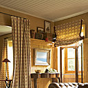 Par une belle fin d’après midi, la lumière vient poser ses rayons afin de réchauffer tout le salon : rideaux , stores, Editions Chotard et carrelage confondent leurs couleurs pour donner le ton à l’ensemble ; accroché au-dessus de la console, Village Notre Dame, un tableau de Paul Vayson (1842-1911), Chesterfield, Village Notre Dame.
