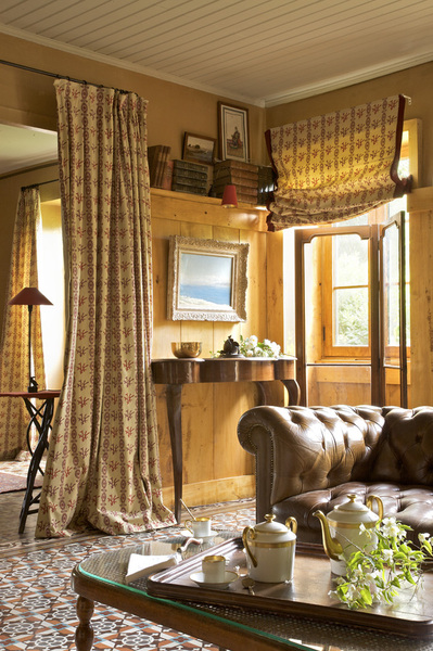 Par une belle fin d’après midi, la lumière vient poser ses rayons afin de réchauffer tout le salon : rideaux , stores, Editions Chotard et carrelage confondent leurs couleurs pour donner le ton à l’ensemble ; accroché au-dessus de la console, Village Notre Dame, un tableau de Paul Vayson (1842-1911), Chesterfield, Village Notre Dame.