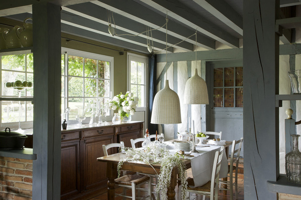 Inondée de lumière, la cuisine s’habille de blanc profitant de la douceur des colombages repeints en bleu cendré, Alto. Sur une table chinée, Village Notre Dame, chemin de table blanc Naaj, CSAO,  vaisselle, Vermont Frères, buffet, Village Notre Dame, posés dessus, objets en verre, Lieux, Habitat, RKR, suspensions, Ikea.