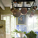 Ouverte sur le jardin,  la pièce profite des rayons du soleil tard le soir. Au-dessous d’une suspension artisanale ornée d’anciennes casseroles en cuivre, une table de drapier XIXème recouverte d’un plateau en granit plus propice à la cuisine ; peinture « Landais », Montes Iturios.