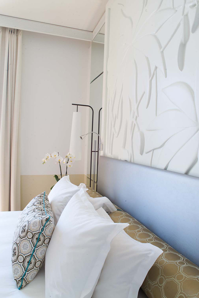 Tête de lit chambre hôtel Royal Riviera. Un grand bas relief en Corian avec un motif évoquant la végétation luxuriante de la Côte d’Azur a été dessiné spécialement et fait office de tête de lit. Les tissus des coussins et oreillers sont des rééditions de tissus des années 50.