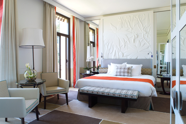 Chambre à l'hôtel Royal Riviera. Le mobilier dessiné pour l’hôtel joue sur les formes courbes des tables de chevet, du miroir (en forme de galet) dans lequel est intégré la télévision. Le bas relief au dessin  de végétation luxuriante, répond aux meubles, bureaux et armoires aux lignes simples mais habillé de miroir. La moquette a été dessinée dans l’esprit  des superpositions de tapis chère aux pays méditerranéens.