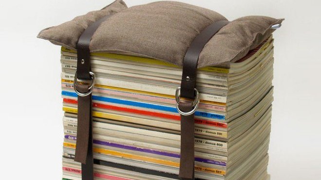 Des revues empilées sur une structure en bois, retenues par 2 sangles