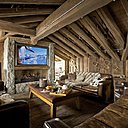 Face à la cheminée en granit, des canapés douillets en cuir habillés de coussins , Winkler,  ont été chinés en Angleterre; Entre les poutres et sur les murs en bois,  servant de décoration, skis et raquettes  anciens ont été  accrochés un peu partout, Chehoma.