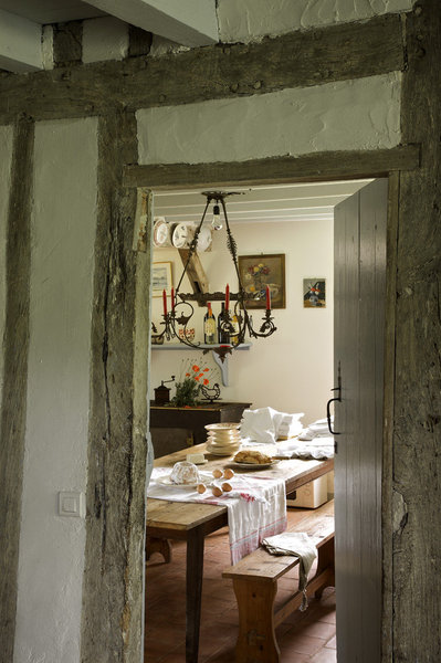 Un salon très cosy vient s’ouvrir sur la cuisine. Linge de table, vaisselle et table de ferme de famille,  ancien fourneau à bois transformé en meuble, au-dessus, nature morte, Léonce Fort.
