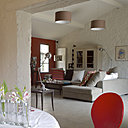 Ambiance très lumineuse pour ce salon salle à manger qui se décline dans des tons d’argile,  passant d’un sol en béton ciré blanc gris se fondant avec des murs en crépit blanc réveillés par un aplat rouge orangé ; peintures et béton ciré, Mercadier. Suspensions, Bellino Lighting, Belgique, canapé, Souplina, coussins, Mia Zia et Ikea, table basse, Déco du Monde, lampe et lampadaire, Jielde, Maison Montigny, vitrine chinée peinte en « London Stone », Farrow &Ball, devant le radiateur, lampadaire, 2B Design.

Côté salle à manger, nappe, Linvosges, vase «  d’avril »  Tsé Tsé chez Sentou galerie, chaises, Fly.