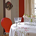 Dans la  salle à manger, l’originalité des murs qui se déclinent en rayures s’harmonisent avec les tommettes au sol couleur bordeaux. Peintures murales bayadère,  Mercadier,  plateau sur le mur, Ibride, applique, Bellino Lighting, rideaux, Ikea, nappe, Linvosges, vase d’avril, Tsé Tsé , Sentou galerie, chaise, Fly.