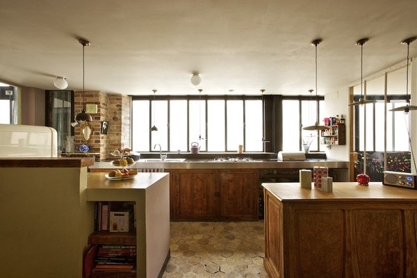 La cuisine s’organise sur deux plans, évier et plaques de cuisson sous la fenêtre, en face, deux blocs compacts qui dissimulent des rangements ; meubles de cuisine, brocante Belle Lurette, suspensions noires, Puces d’Orléans à droite Emmaüs.
