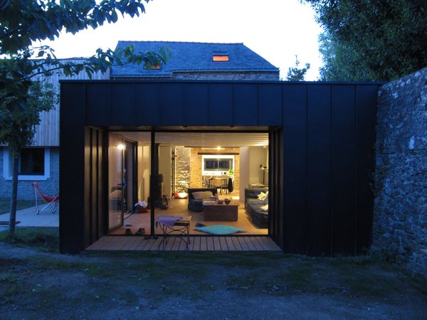 Le salon s’ouvre sur le jardin par une large baie cadrant la vue et protégé du soleil estival par un débord de toiture.
