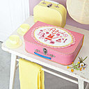 Un joli alphabet brodé sur un tissu façon napperon et appliqué sur une valisette d'enfant rose, pour accueillir robes de poupée et petits trésors de demoiselle.