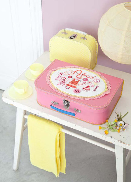 Un joli alphabet brodé sur un tissu façon napperon et appliqué sur une valisette d'enfant rose, pour accueillir robes de poupée et petits trésors de demoiselle.