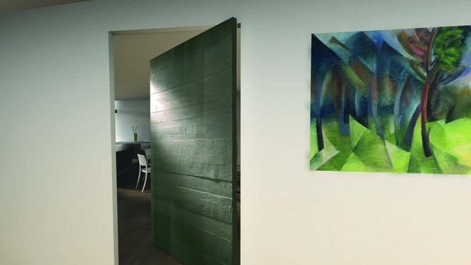 Habillée de béton mélangé à de la résine, la large porte sur pivot devient un élément architectural important