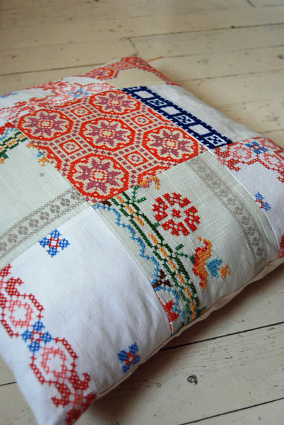 Coussin à l'aspect scandinave résolument moderne, composé de pièces de tissus brodés, découpées dans des nappes anciennes.