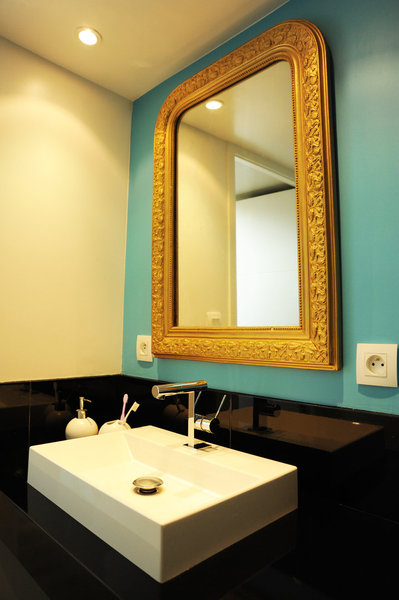 Dans la salle de bains, un miroir chiné et redoré contraste avec un mur turquoise, la blancheur d’un lavabo en acrylique et la modernité d’un meuble sous vaque laqué noir, réalisé sur mesure.