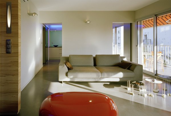 Elément essentiel de la transformation de l’espace pour Isabelle Marion, la lumière du soleil vient sculpter l’espace, en se reflétant sur la table rouge Koishi de Naoto Fukasawa. Les spots Aixlight de Declic apportent une lumière douce, qui invite à s’installer confortablement sur le canapé Malcom de Calligaris.