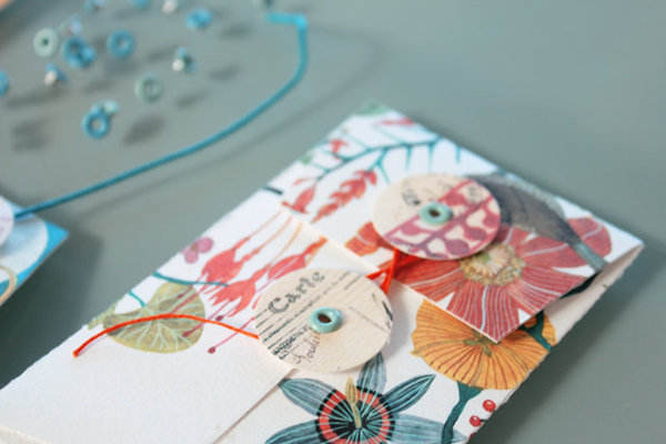 Deux cercles découpés à la perforatrice fixés avec un oeillet sont reliés et fermés par un lien de couleur.