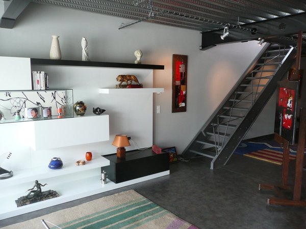 Le salon joue la carte de la simplicité graphique avec une bibliothèque murale combinant étagères ouvertes et rangements fermés, décalés.