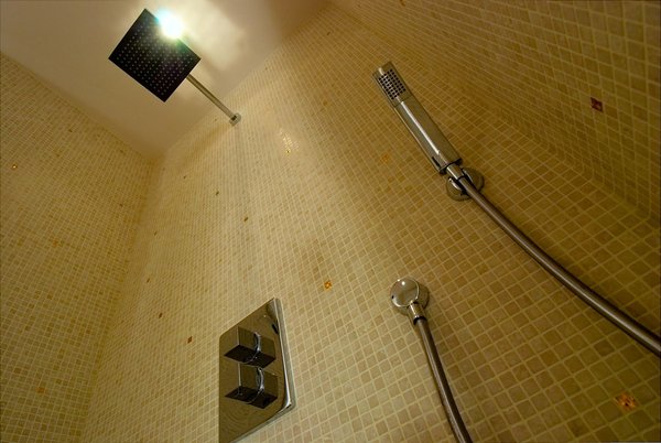 Cabine de douche nappée d’une mini-mosaïque de tesselles de marbre blanc cassé aux accents rosé (1 cm de côté) ponctuée de carreaux dorés.