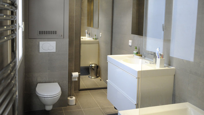 Dans la salle de bains, on a rajouté un coin toilettes avec une cuvette suspendue et une chasse d’eau encastrée dans le mur. Nappée de grès cérame, l’espace est doté d’un miroir qui agrandit l’espace.