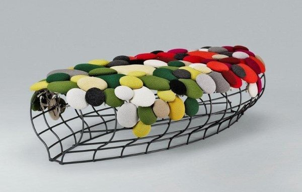 Grand pouf en mailles métalliques rendu confortable par une multitude de coussins pastilles, signés Katrin Sonnleitner.