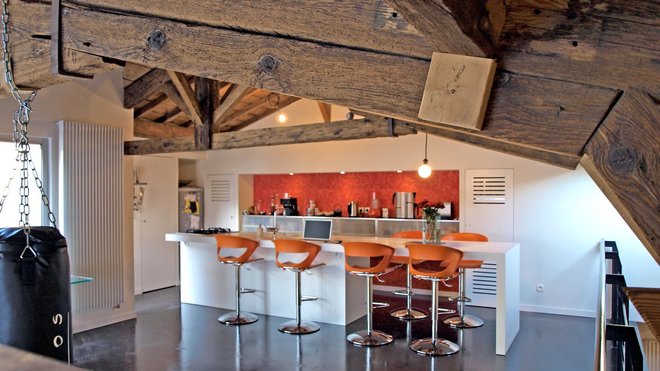 Côté cuisine, deux aménagements parallèles se font face : Un comptoir façon bar qui sert de coin repas et de plan de travail ; un mur de placards linéaires qui encadrent une niche. La chaudière est camouflée derrière l’une des façades ajourées, aménagées en éléments symétriques de finition.