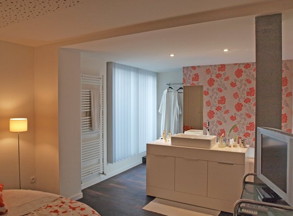 La cloison, qui sépare l’espace douche du reste de la salle de bains est recouverte d’un panneau de papier peint. Pour accéder à la terrasse surélevée, une  marche rattrape le niveau de la douche à l’italienne, camoufle le système d’évacuation et offre un espace supplémentaire pour se sécher.