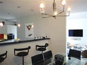 La cuisine semi-ouverte avec son bar et à été conservée. Elle dessine désormais un espace graphique en noir et blanc. Dans la salle à manger, table Jérôme Guimier. Lustre et chaises, Bô.