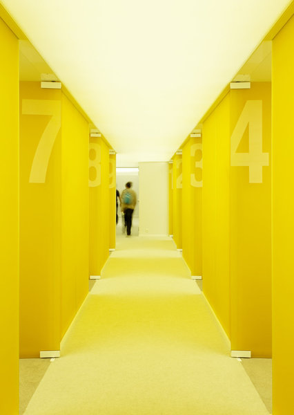 Enfilade de bureaux et salles de réunion cloisonnés de verre jaune sablé.