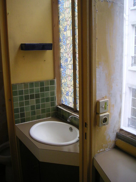 Avant : une salle de bains aux teintes discordantes, sans rangement, équipée d’une minuscule vasque. Des murs mal isolés avec une verrière partiellement camouflée derrière un décor adhésif.