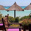 La terrasse de l'hôtel surplombe la plage de Santa Giulia. Parasols en brandes de bruyère dans un esprit tropical.