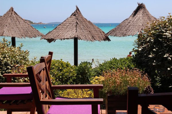 La terrasse de l'hôtel surplombe la plage de Santa Giulia. Parasols en brandes de bruyère dans un esprit tropical.