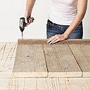 Etape 2 : Pour construire le côté gauche du banc comme pour le côté droit, disposer les trois planches découpées côte à côte sur une surface plane, puis utiliser le tournevis (ou la visseuse) et les vis auto-foreuses. Fixer la lambourde à ras des planches.