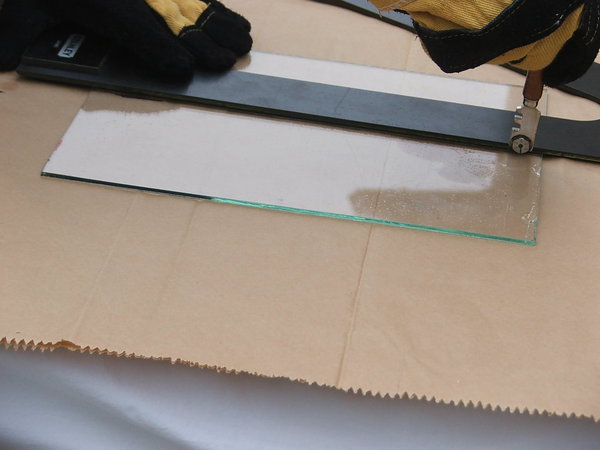 Etape 5 : Muni de gants, placer le coupe-verre à 2 mm à l’intérieur de la feuille de verre. L’outil devra être tenu bien perpendiculairement à la surface de coupe, et surtout bien pris en main.