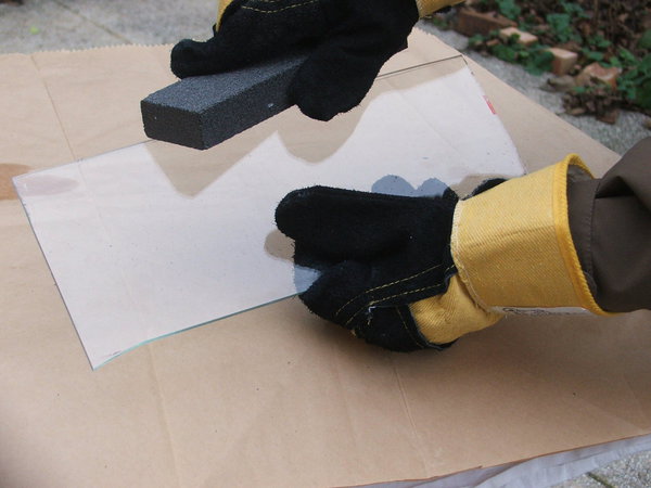 Etape 9 : Dans le but d’abattre les arrêtes du verre, prendre une pierre de  carborundum  légèrement  mouillée à l’eau claire, et passer sur la coupe ; Tenir la pierre légèrement inclinée en passant un geste continu sans trop appuyer, et sans arrêt sur les deux faces. Renouveler l’opération plusieurs fois de suite jusqu’à l’obtention d’un résultat parfait et sans aspérités.