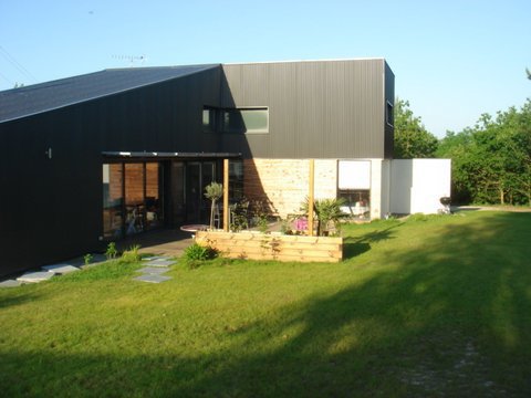 La maison est recouverte d’un bardage métallique gris argenté. La couverture s’harmonise avec des parois.