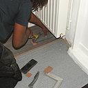 Etape 15 : Emboîter la nouvelle lame de stratifié dans la rainure de l’avant dernière, en la cliquant par une simple pression des deux mains. Puis avec un tire lame placé en bout de plinthe, taper un léger coup au marteau, renforçant ainsi la liaison entre les lames.