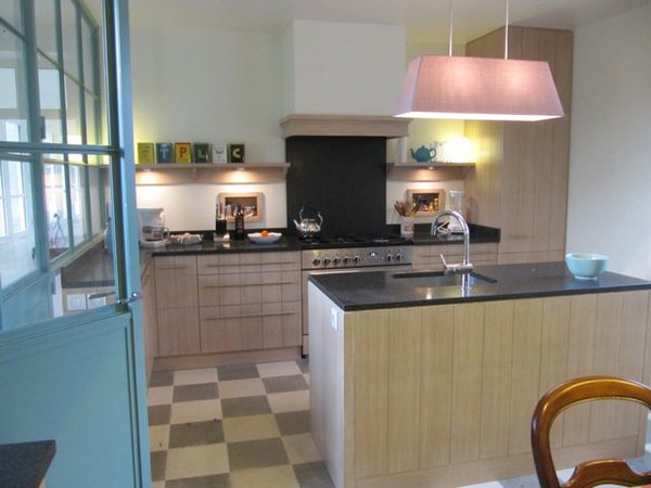 La cuisine au sol bicolore nappé d’un damier de pierre de Dordogne dessine un espace lumineux. Les éléments de rangement en plaquage de chêne cérusé et blanchi, ont été réalisés sur mesure. Leurs façades offrent des panneaux rainurés imitant un assemblage de planches massives. Le plan de travail est en granit.